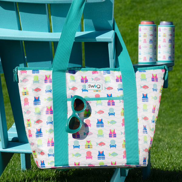 Swig Life Lake Girl Insulated Zippi Cooler on a teal adirondack chair next to two Skinny Can Coolers